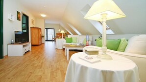 A spacious living room with a television, a dining area with a table and chairs, and a cozy seating area with a lamp.