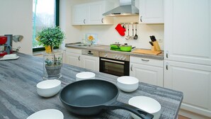 A modern kitchen with white cabinets, a stove, a sink, and a countertop with bowls and a frying pan.