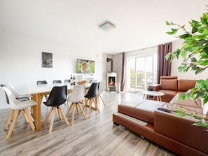 Una sala de estar moderna con un sofá, una mesa de comedor con sillas, una chimenea y un ventanal grande.
