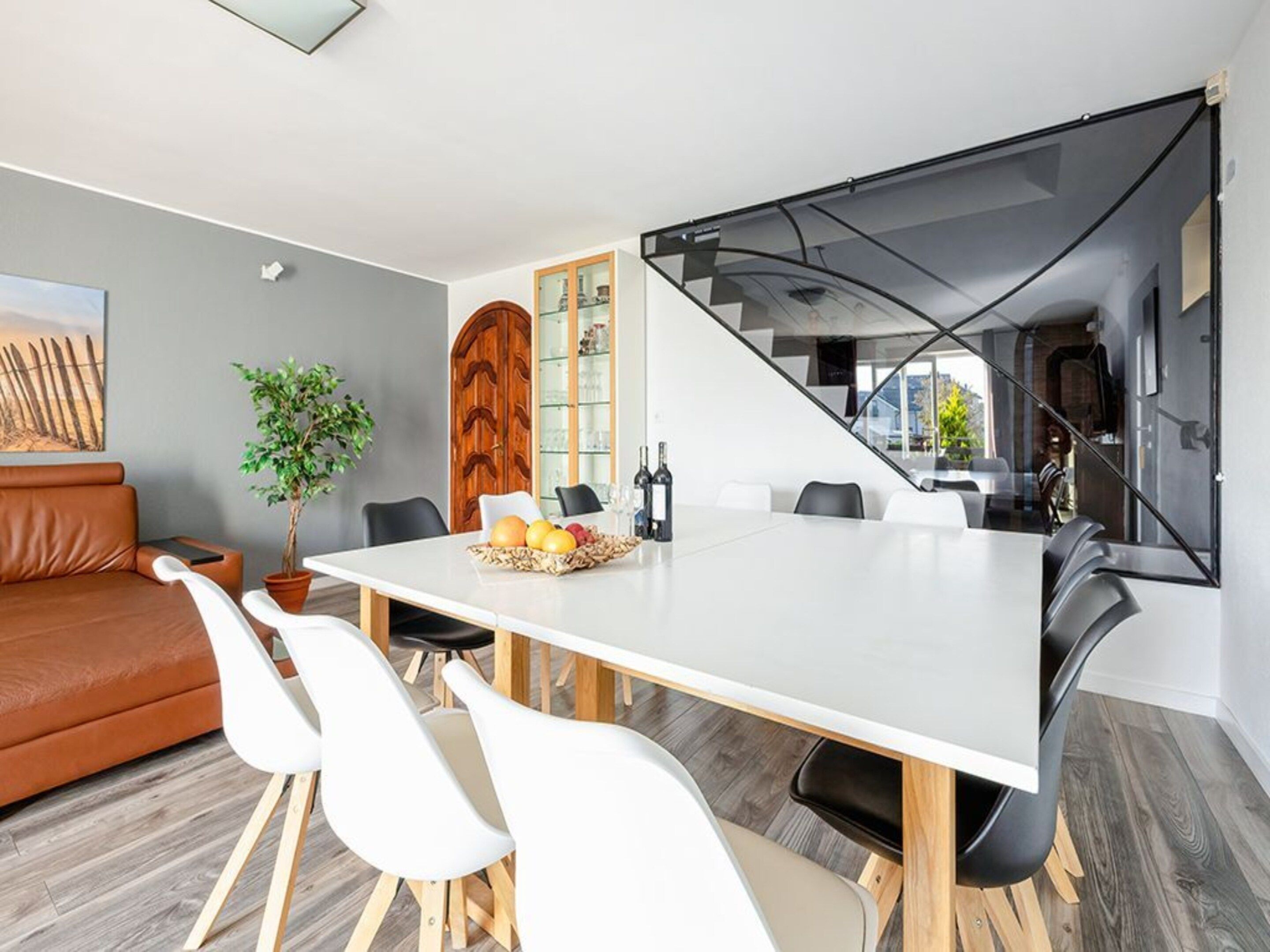 Uma área de refeições moderna com uma mesa branca, cadeiras pretas e um armário de madeira.