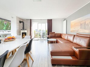Una sala de estar moderna con un sofá de cuero, una mesa de comedor con sillas, una chimenea y un ventanal con cortinas.