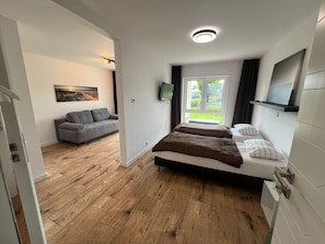 Un dormitorio con cama, televisor, ventana con vistas y un sofá en la habitación contigua.