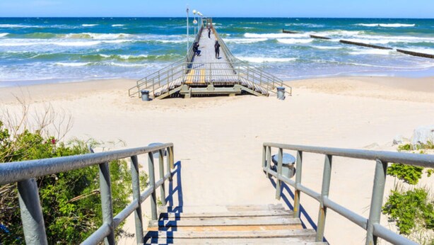 A wooden pier leading to a lifeguard tower on a beach with waves in the background. - Terraced Houses in Sarbinowo Near Beach (Mielno)