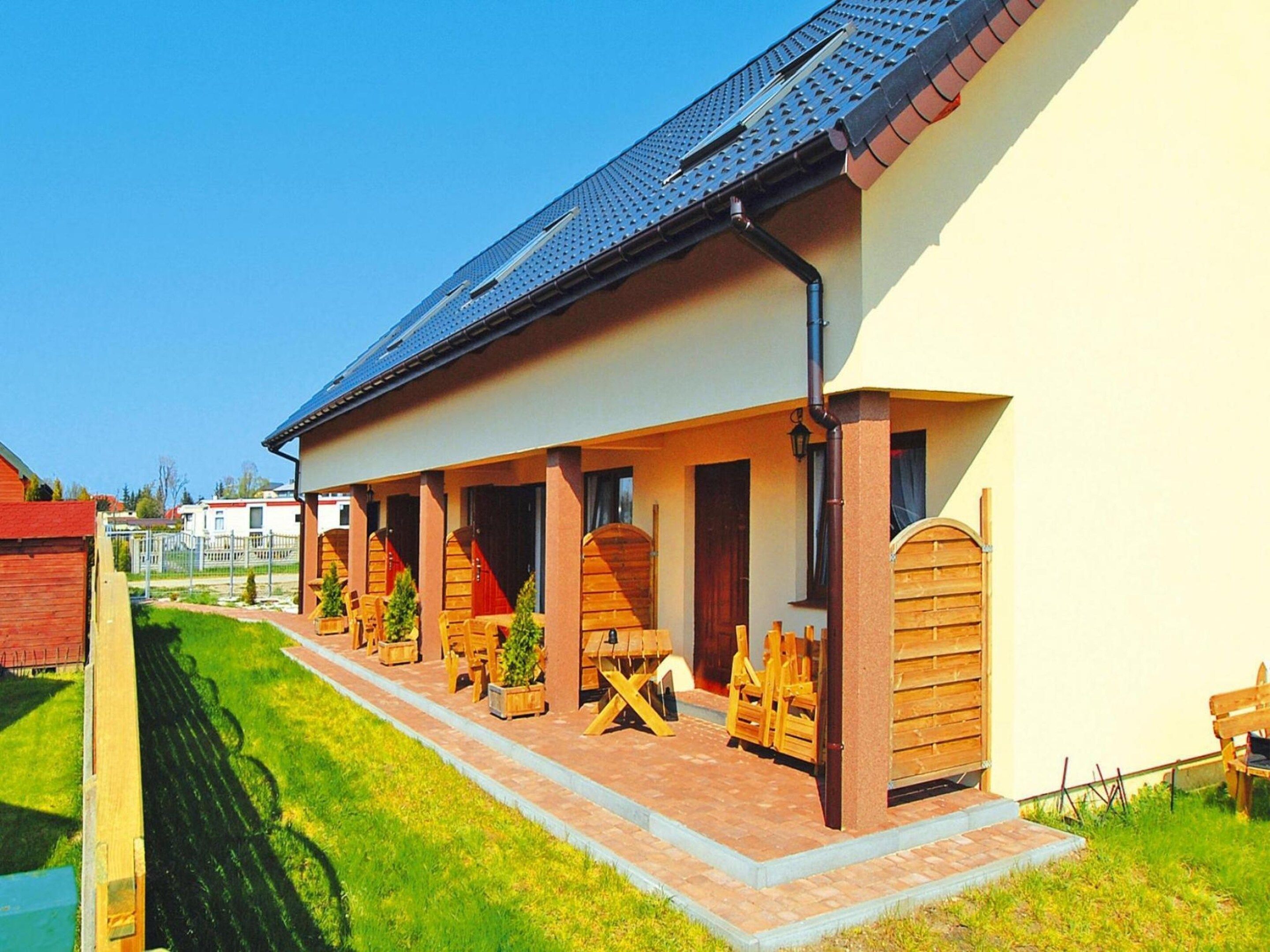 A building with a covered porch, wooden furniture, and a clear sky.