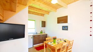 A compact kitchen with a wooden ceiling, a dining table with chairs, and a flat-screen TV mounted on the wall. - Terraced Houses in Sarbinowo Near Beach (Mielno)