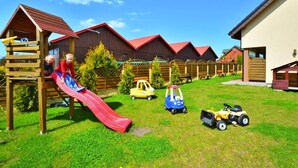 A playground with a red slide, wooden play structures, and toy vehicles. - Terraced Houses in Sarbinowo Near Beach (Mielno)