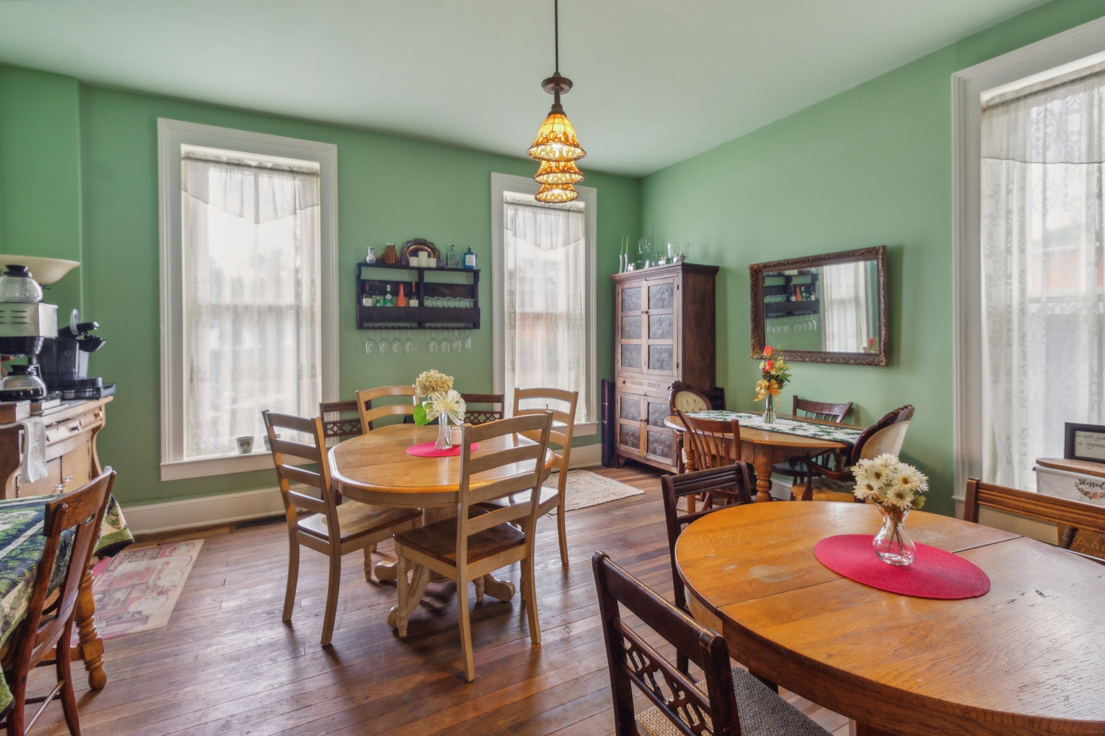 A dining room with wooden tables and chairs, a chandelier, and a cabinet with glassware.