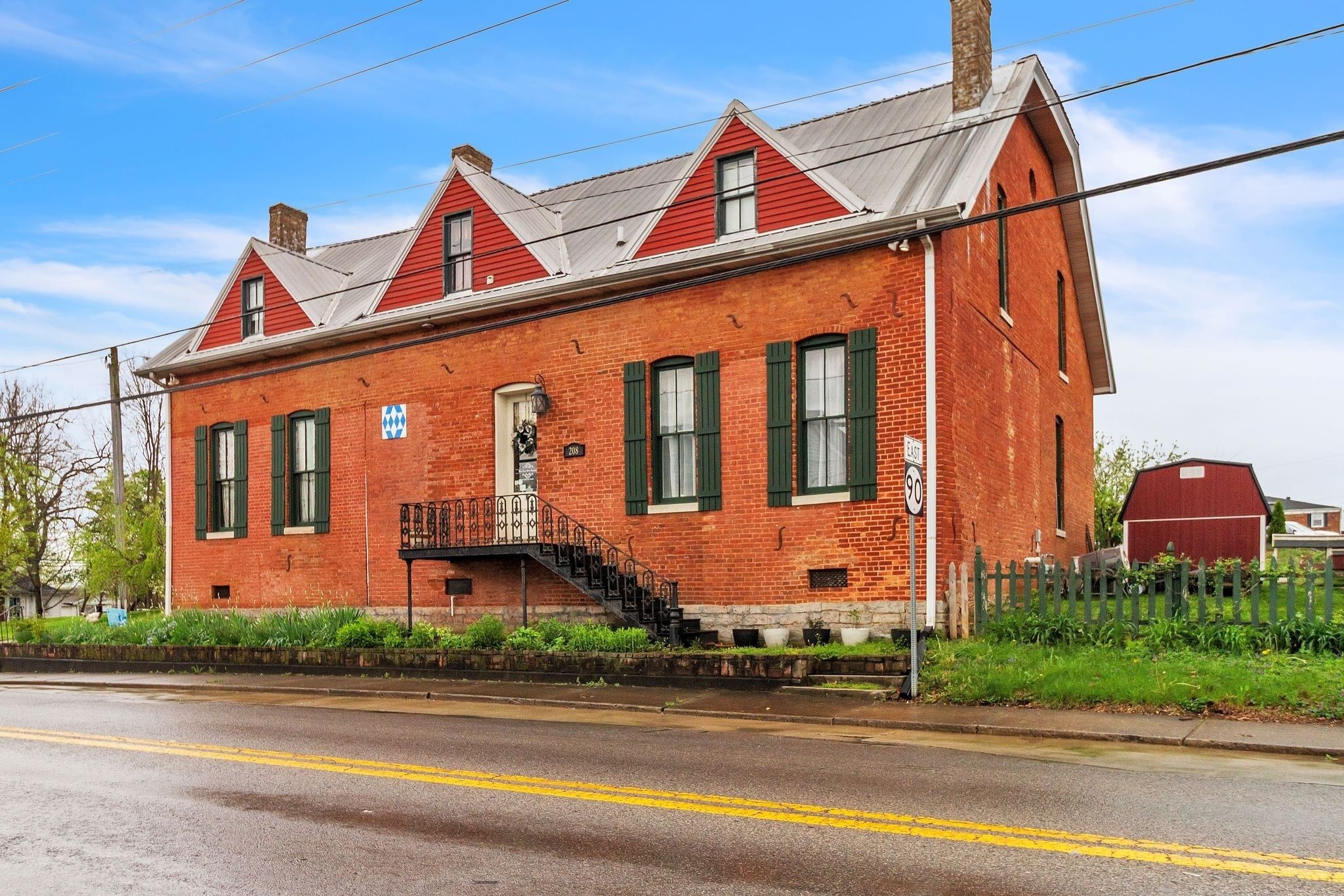 A red brick building with green shutters, a front staircase, and a street sign indicating a 90 mph speed limit.