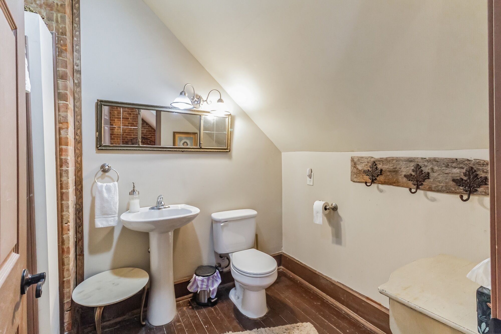Ein Badezimmer mit weißem Waschbecken, WC und Bidet, einem Spiegel mit Beleuchtung sowie einem rustikalen Holzregal.