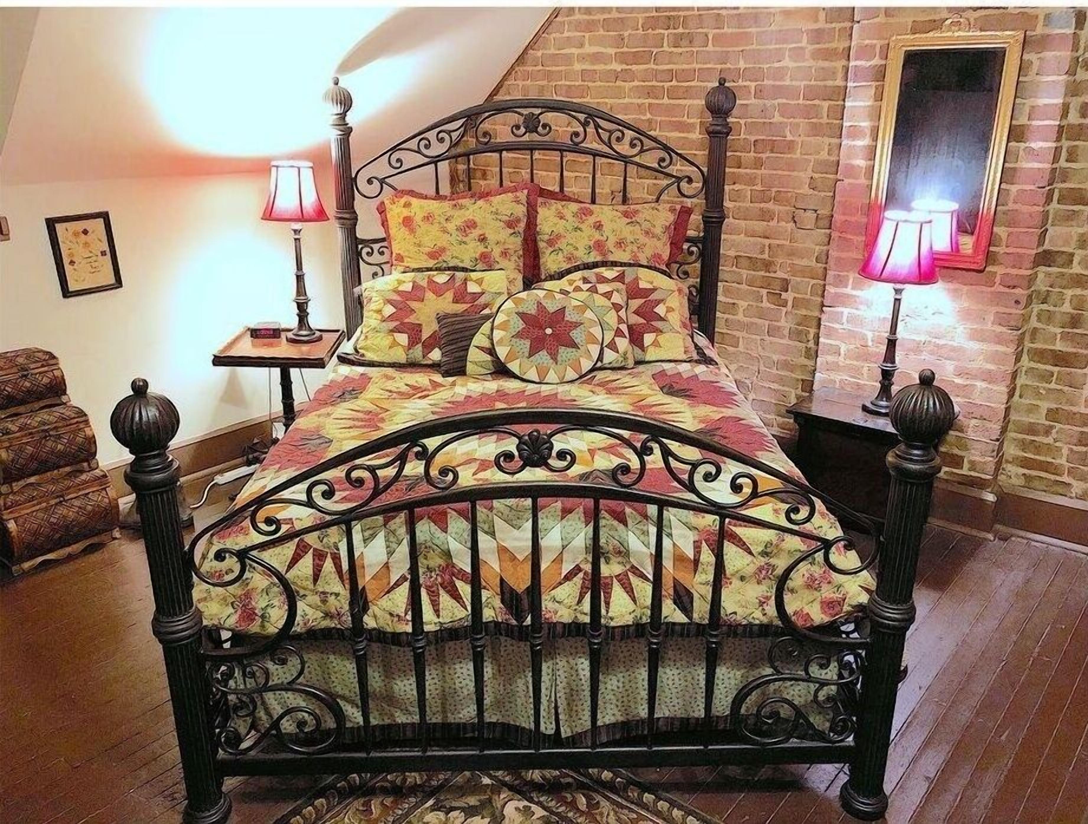 Un dormitorio con pared de ladrillo, una cama con colcha floral, dos lámparas de noche y una silla.