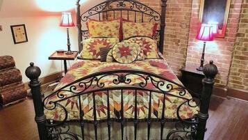 Un dormitorio con pared de ladrillo, una cama con colcha floral, dos lámparas de noche y una silla.
