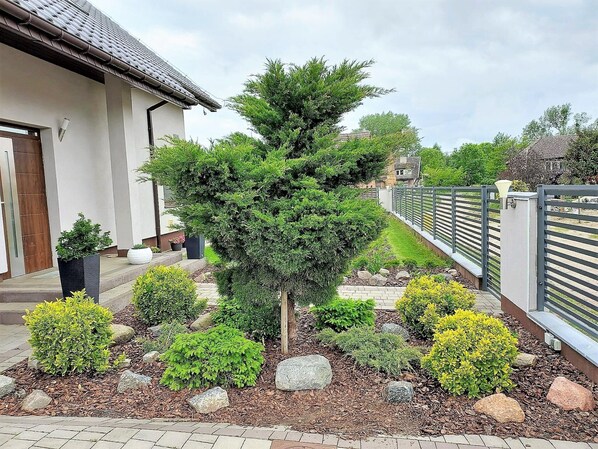Un jardin aménagé avec différents arbustes et un petit arbre devant une maison.
