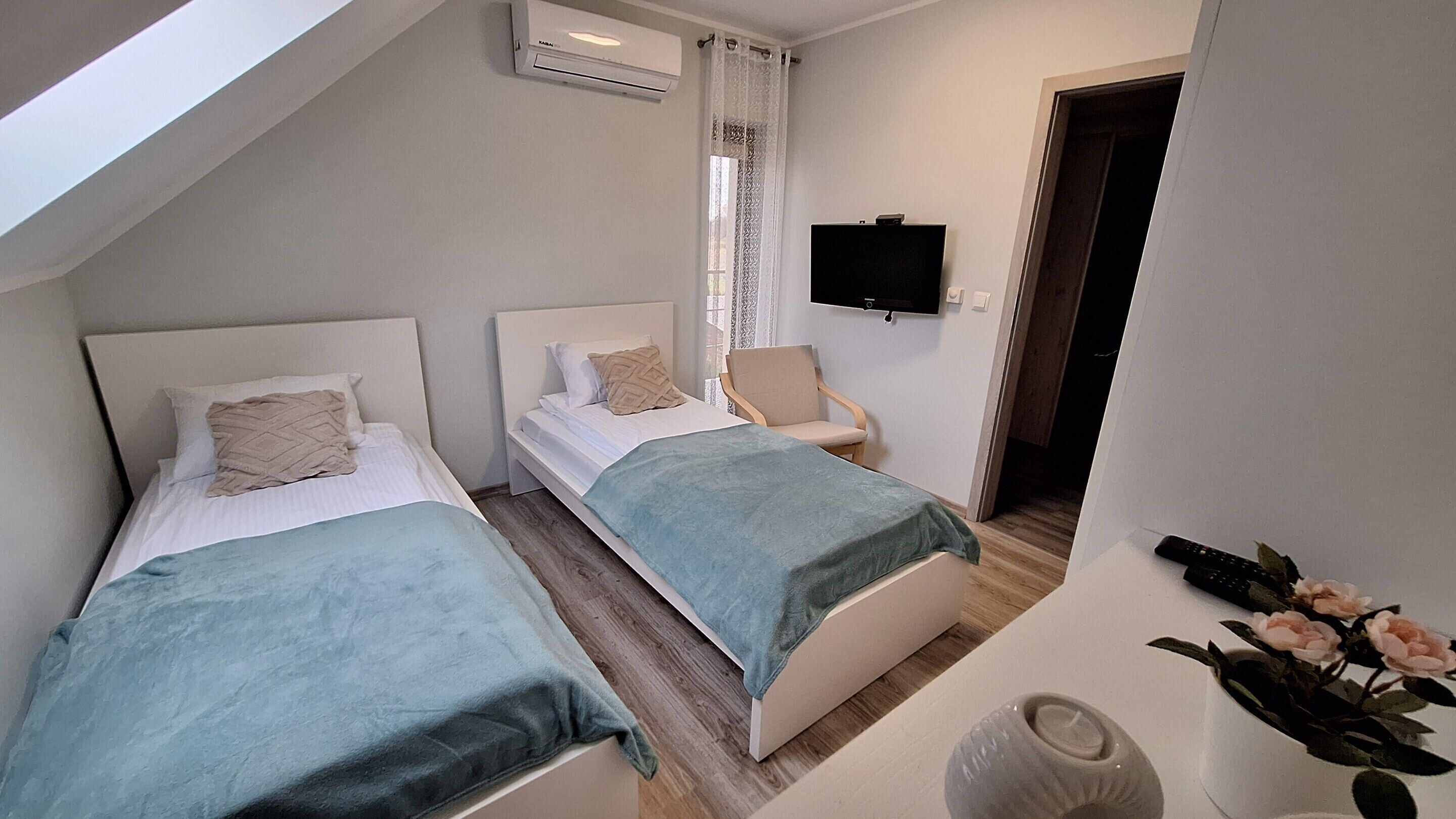 Une petite chambre moderne avec deux lits, une télévision et une fenêtre avec des rideaux.