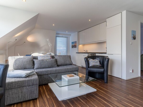 A modern living room with a grey sofa, a glass coffee table, and a black leather armchair. - Wohnung in St. Peter Ording (St. Peter-Ording)