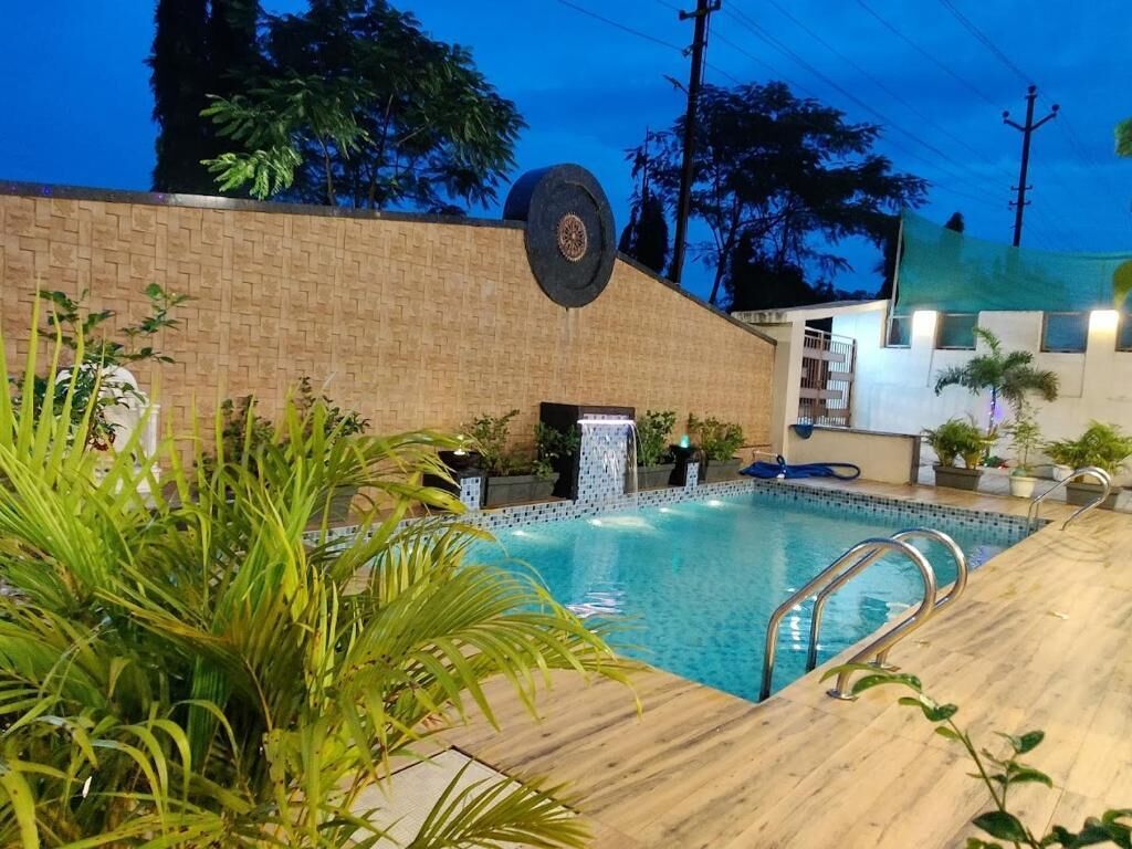 A swimming pool with a wooden deck, surrounded by potted plants and a brick wall.