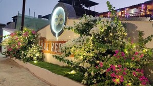L’entrée d’un hôtel, avec une grande enseigne lumineuse, des arbustes luxuriants en fleurs et un chemin bien éclairé.