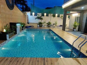A swimming pool with a tiled edge, a wooden deck, and a metal ladder. - Raj Heritage Ghorle By GRB (Murbad)
