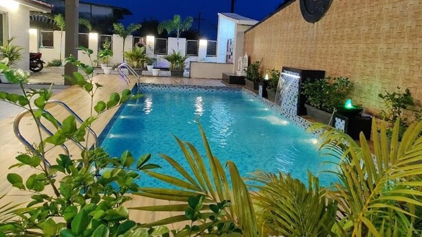 Une piscine agrémentée d’un élément décoratif aquatique, entourée de plantes en pot et d’un mur de briques.
