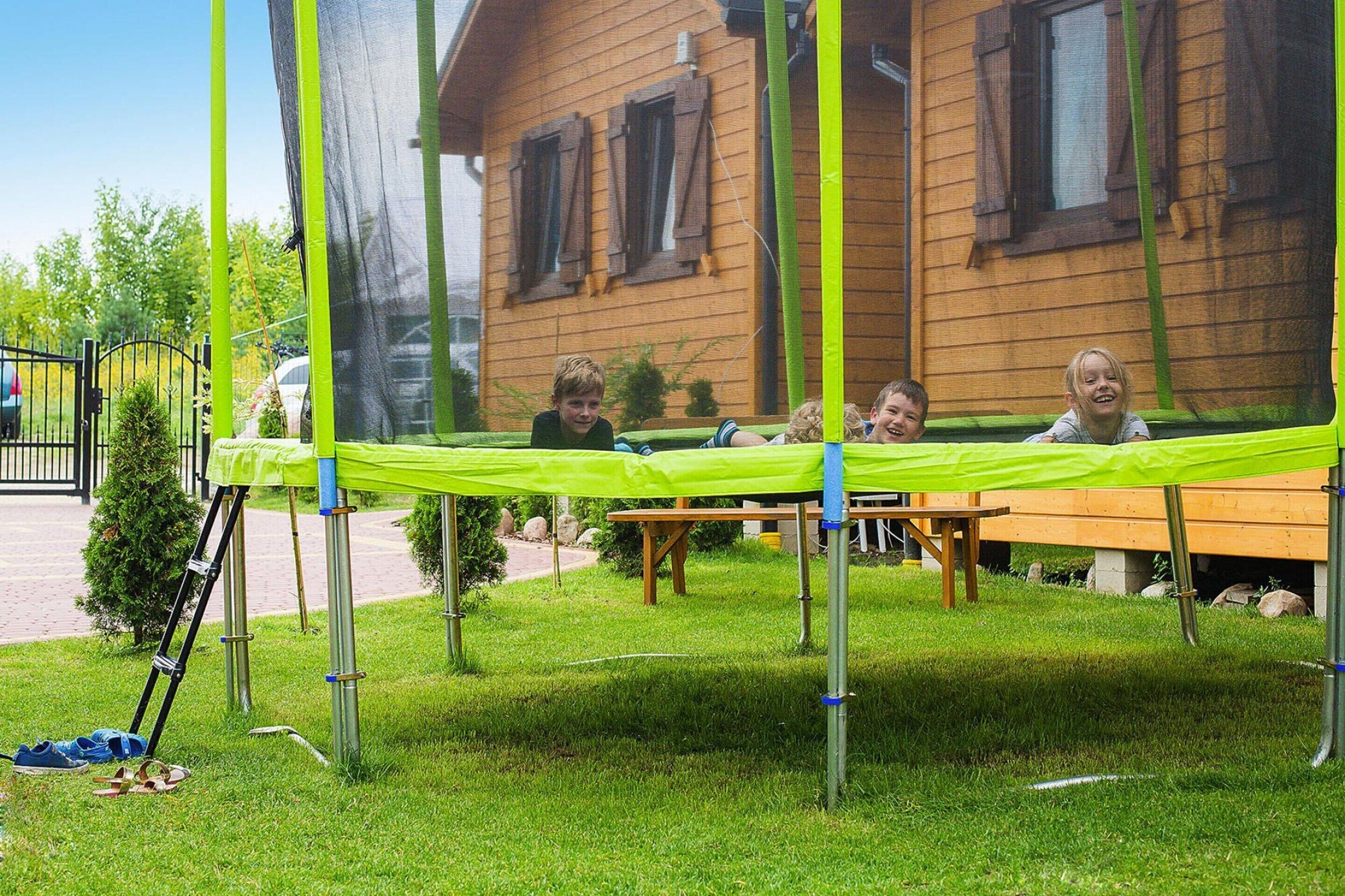 Ein Holzhaus mit einem grünen Trampolin auf einer Rasenfläche.