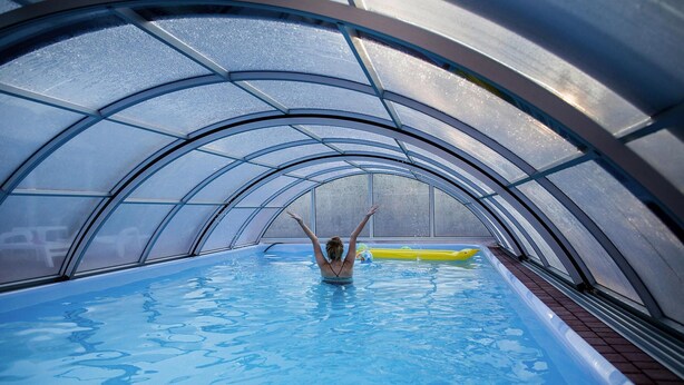 Une piscine dotée d’un toit en verre, une personne dans l’eau et un flotteur jaune.
