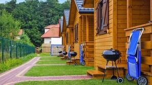 Une rangée de cabanes en bois, chacune équipée d’un barbecue et d’une chaise pliante bleue.