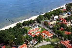 Vue aérienne d’une ville côtière avec une plage, des immeubles résidentiels et un grand bâtiment doté d’un toit rouge.