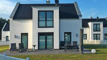 A modern two-story house with a flat roof, large windows, and a patio area with outdoor furniture.