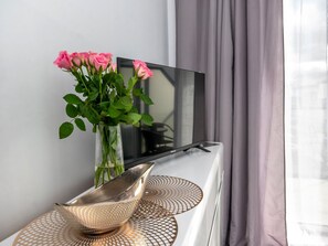 A modern room with a flat-screen TV on a white stand, a vase with pink flowers, and a decorative bowl on a textured surface. - Holiday Studio for 3 People, Dziwnow (Dziwnów)