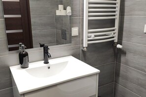 A bathroom with a white sink, a mirror, a towel rack, and a shower area. - Holiday Studio for 3 People, Dziwnow (Dziwnów)