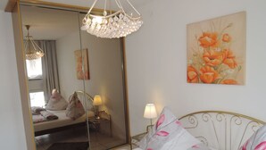 A bedroom with a large mirror, a chandelier, a bed with floral bedding, a bedside table with a lamp, and a painting of flowers on the wall. - Apartment in Misdroy Near Baltic Beach (Międzyzdroje)
