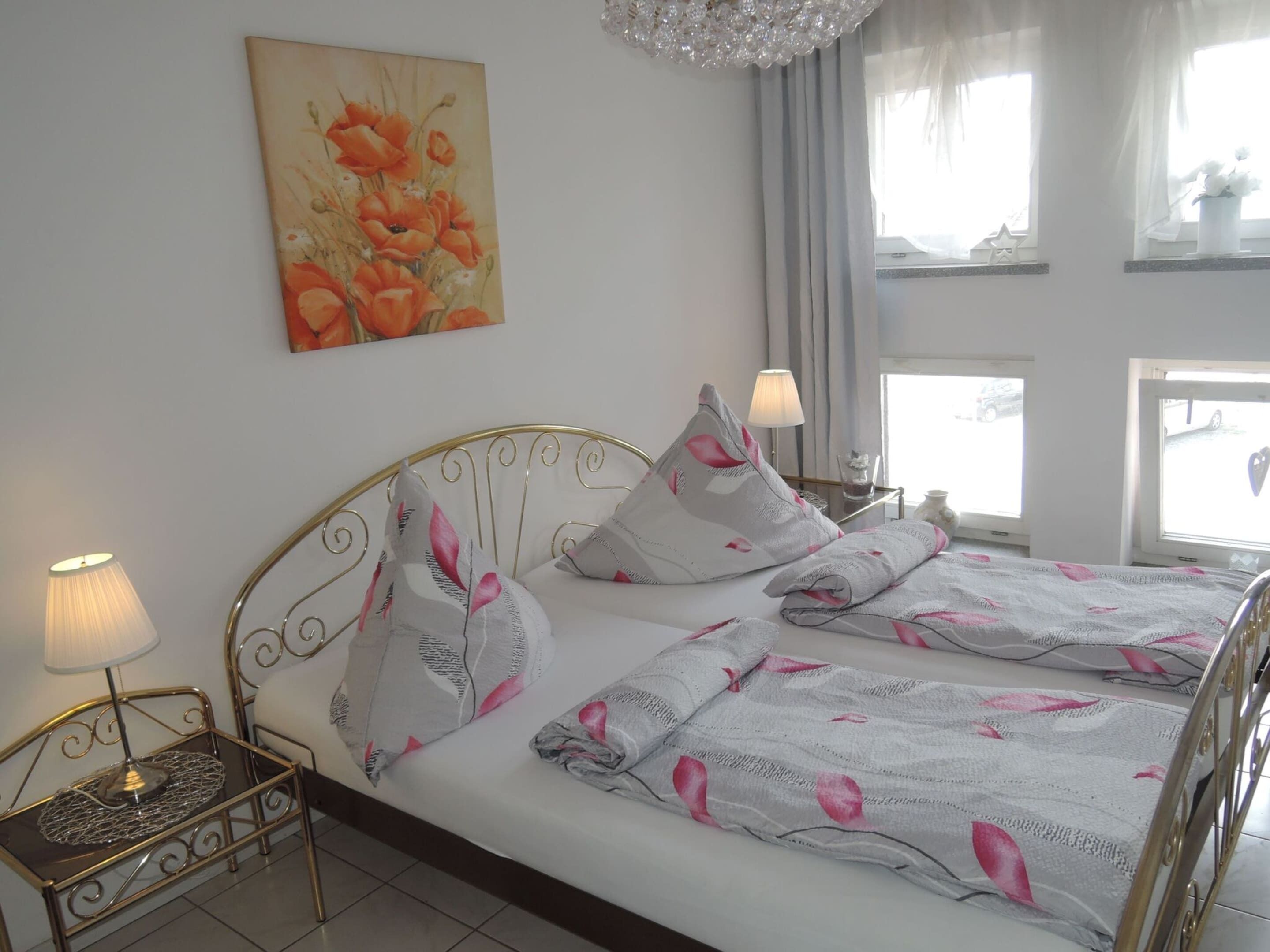 A neatly made bed with floral bedding, a bedside table with a lamp, and a painting on the wall.