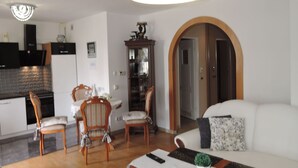 A modern living room with a white sofa, wooden chairs, a dining table, and a kitchen area with cabinets and a built-in oven. - Apartment in Misdroy Near Baltic Beach (Międzyzdroje)