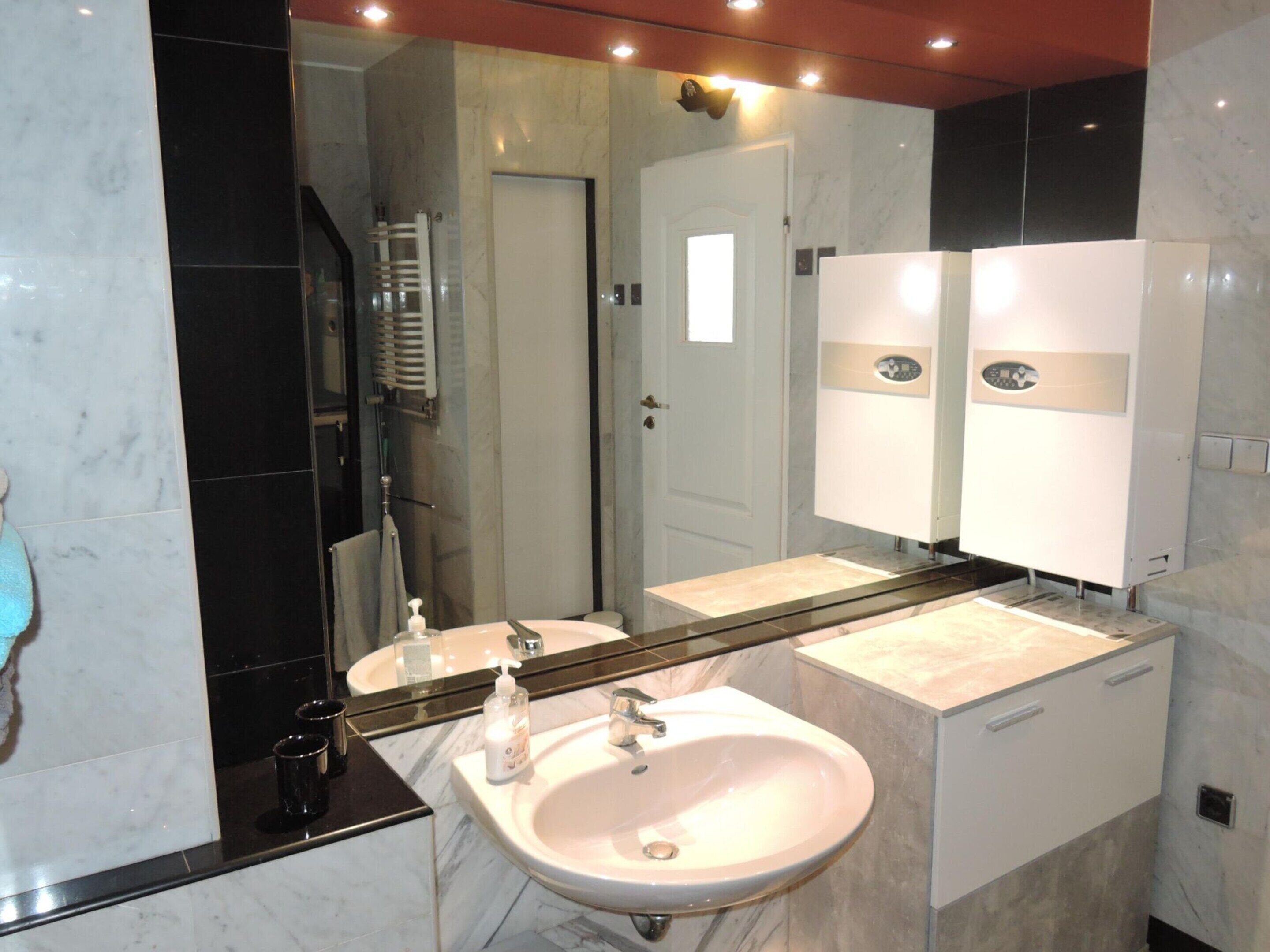 Une salle de bain moderne avec un grand miroir, deux lavabos, une douche et un porte-serviettes.