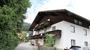 Ein traditionelles Chalet mit geneigtem Dach, hölzernen Balkonen und einer Steinwand.