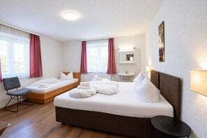 A hotel room with a large bed, a smaller bed, a desk, a chair, a bathroom with a sink and mirror, and a window with curtains.