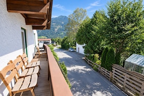 Una terraza de madera con bancos que da a una calle con casas y una montaña al fondo.