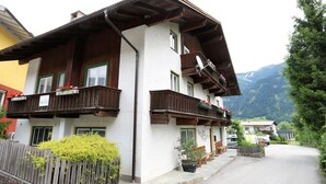 Ein traditionelles Chalet mit hölzernen Balkonen, einem Steinzaun und einem Berg im Hintergrund.
