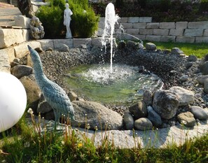 Un jardín con una fuente, una estatua y un estanque rodeado de rocas y plantas.