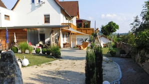 A two-story house with a covered patio, a small garden with rocks and plants, and a gravel driveway. - Apartment in Veringendorf Near Swabian Alb (Veringenstadt)
