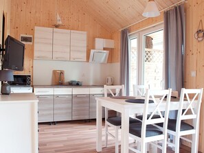 A compact kitchen with wooden cabinets, a microwave, a kettle, and a dining area with white chairs and a table. - Cottage Near the Sea, Pobierowo (Rewal)