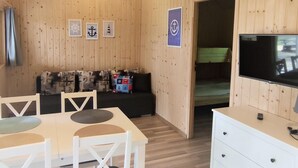 A wooden-paneled room with a sofa, a dining table with chairs, a TV, and a dresser. - Cottage Near the Sea, Pobierowo (Rewal)