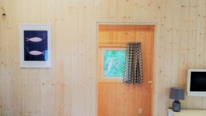 A wooden-paneled room with a window, a framed picture of fish, a lamp, and a TV on a cabinet. - Cottage Near the Sea, Pobierowo (Rewal)
