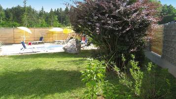 A backyard with a swimming pool, lounge chairs, and a wooden fence.