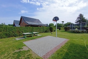 A backyard with a basketball hoop, a picnic table, and a solar panel house in the background. - Holiday Apartment in Kopalino (Choczewo)