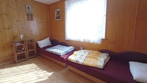 A room with wooden walls, a bed with a purple mattress, a white pillow, and a window with a white curtain. - Holiday Apartment in Kopalino (Choczewo)