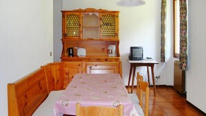 A cozy dining area with a wooden bench and table, a cabinet with glass doors, a small table with a television, and a window with curtains. - Apartment Santa Lucia in Bezecca (Ledro)