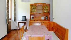 A small kitchen with wooden cabinets, a table with a checkered tablecloth, a chair, a television, and a hanging light fixture. - Apartment Santa Lucia in Bezecca (Ledro)
