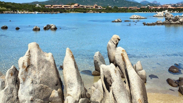 Eine Küstenlandschaft mit klarem, blauem Wasser, Felsformationen und einem fernen Gebirgszug.