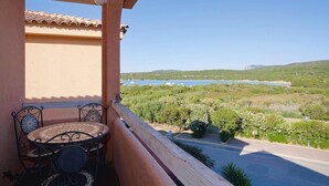 Ein Balkon mit Tisch und Stühlen mit Blick auf eine Küstenlandschaft mit Grünflächen und einem Gewässer.
