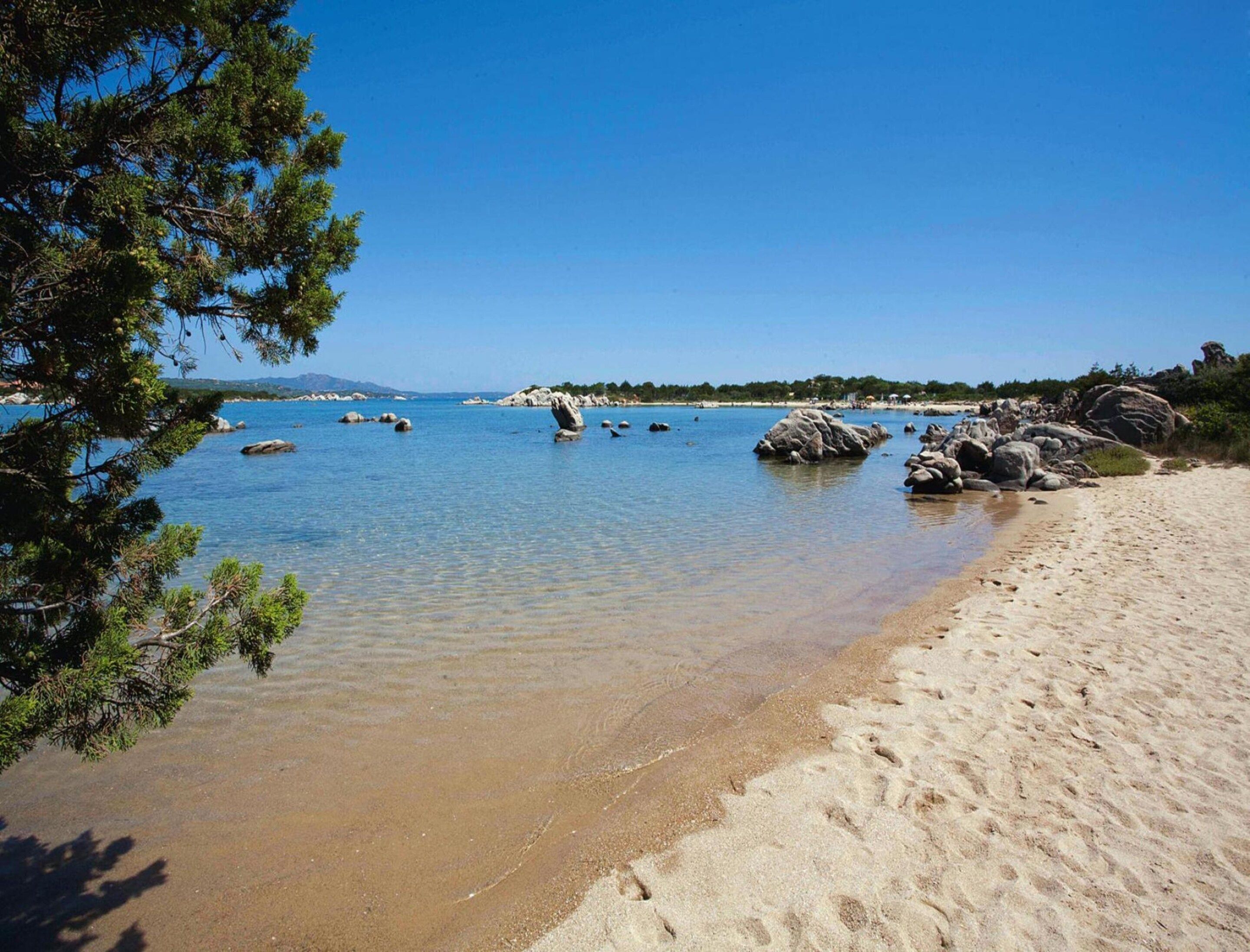 A beach with clear water, rocks, and a sandy shore.